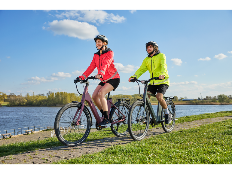 Ein Mann und eine Frau fahren auf einem gepflasterten Weg am Wasser Fahrrad.