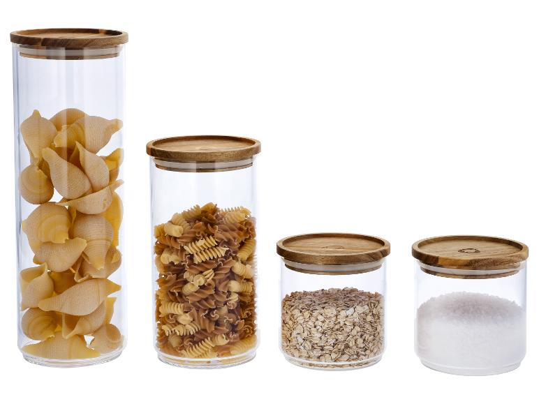 Vier Glasgefäße mit Holzdeckeln, gefüllt mit Nudeln, Haferflocken und Salz.