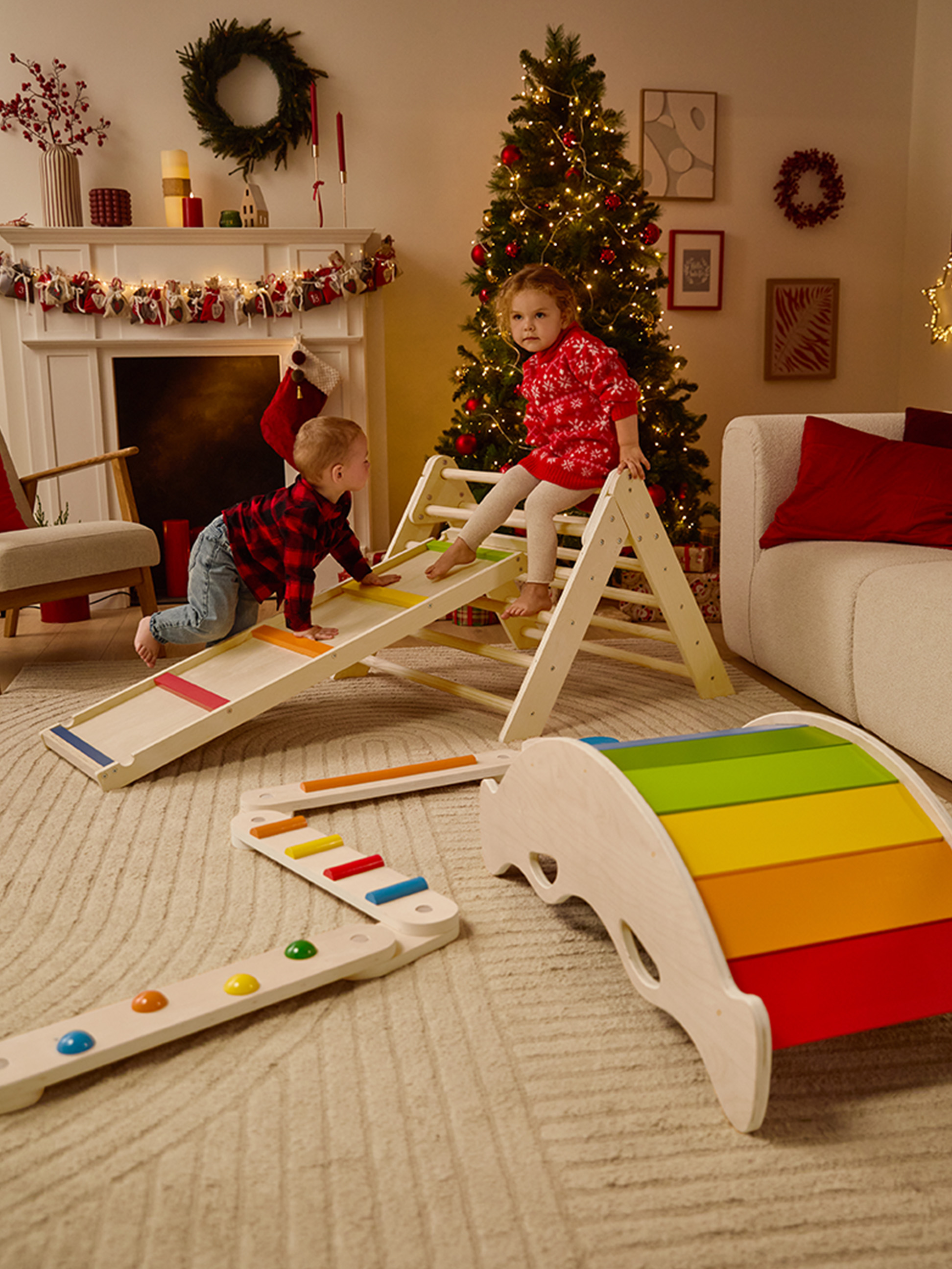 Zwei Kinder spielen auf hölzernen Kletterspielzeugen in einem weihnachtlich dekorierten Wohnzimmer.
