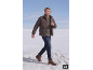 Mann in brauner Daunenjacke, grünem Pullover und Jeans, der durch den Schnee geht.