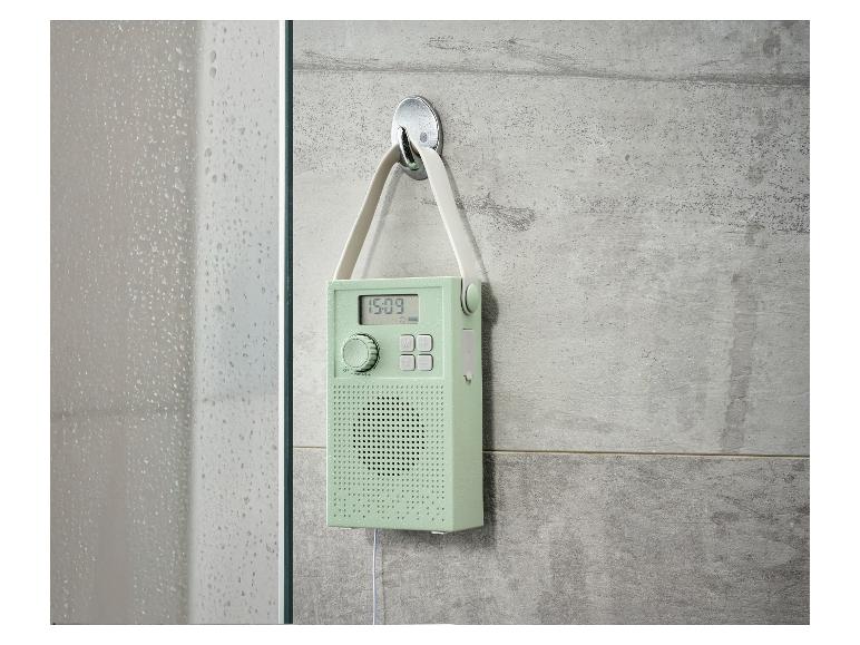 Mintgrünes Duschradio mit Digitalanzeige hängt an einer gefliesten Wand.