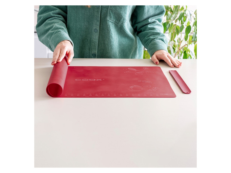 Eine rote Silikon-Backmatte von Coox, aufgerollt auf einem Tisch