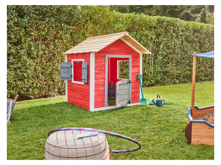 Rotes Holzspielhaus mit Sandkasten und Outdoor-Spielzeug in einem grünen Garten.