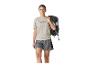 Frau in beigem T-Shirt mit Bergmotiv und grauen Shorts, mit schwarzem Rucksack auf der Schulter.