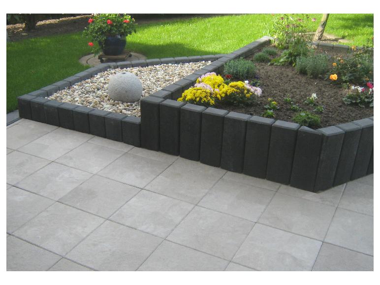 Geflieste Terrasse mit erhöhten Beeten aus dunklen Steinen, gefüllt mit Kies und Blumen.