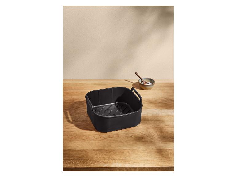 Schwarzer Heißluftfritteusenkorb auf einem Holztisch mit einer kleinen Salatschale.