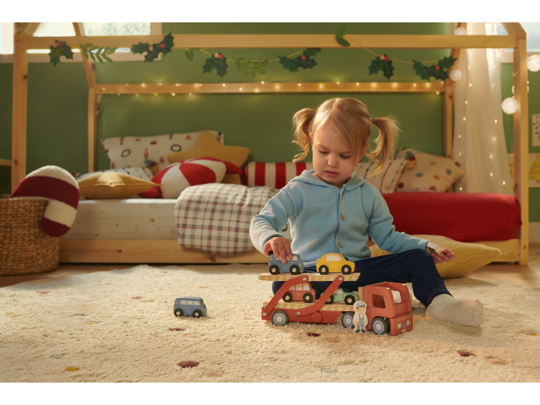 Mädchen spielt mit Holzspielzeug-Autotransporter in weihnachtlich dekoriertem Kinderzimmer.