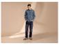 Mann in Jeanshemd und Jeans mit Händen in den Taschen, blickt nach unten.