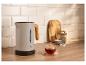 Moderner Wasserkocher mit Holzgriff, eine Tasse Tee und Teezubehör auf einer Holztheke.