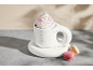 Heiße Schokolade mit Schlagsahne und Streuseln, mit zwei Macarons auf grauem Untergrund.