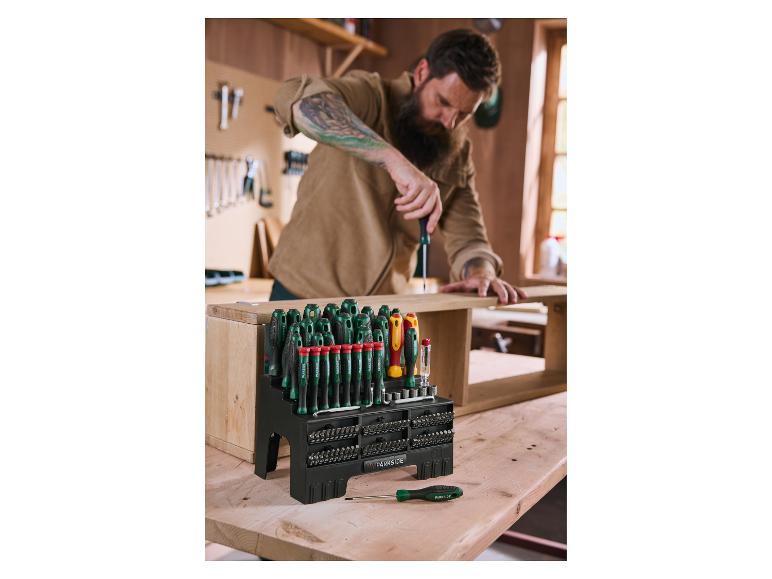 Ein Mann benutzt einen Schraubendreher aus einem großen Set von Schraubendrehern und Bits auf einer Holzwerkbank.