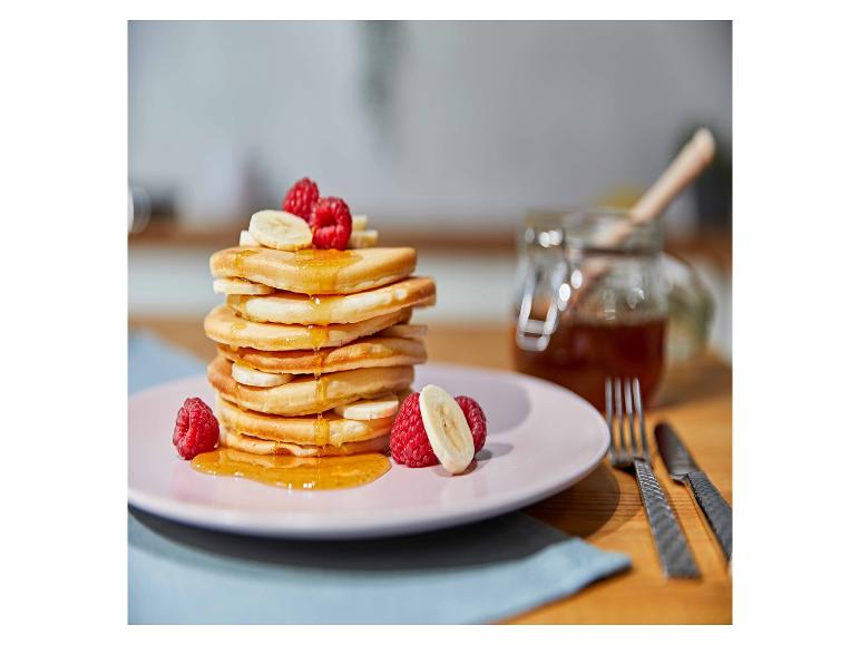 Stapel Pfannkuchen mit Banane, Himbeeren und Honig auf einem rosa Teller.