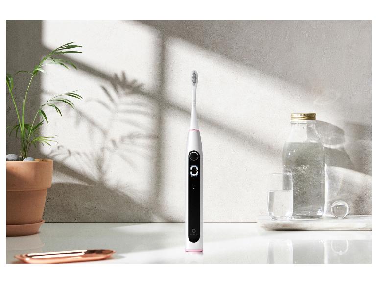 Eine Oclean elektrische Zahnbürste, ein Glas und eine Wasserflasche.