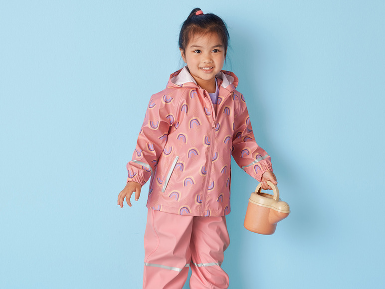 Ein Mädchen trägt einen Regenmantel mit Regenbogenmuster und hält eine Gießkanne.