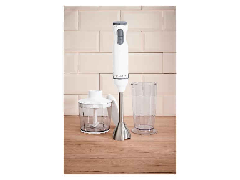 Weißer Stabmixer mit Zerkleinereraufsatz und Messbecher auf einer Holzoberfläche.