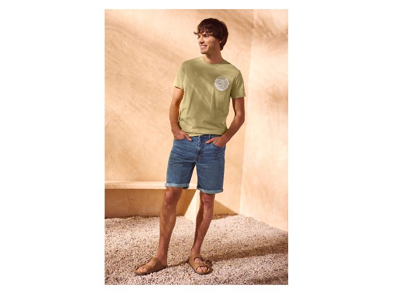 Mann in grünem 'Summer Wave' T-Shirt und Jeans-Shorts.