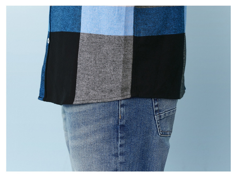 Ein Mann trägt ein blaues kariertes Hemd und Jeans.