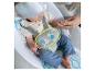 Baby in Wippe mit Elefantenspielzeug, hält die Hand eines Erwachsenen.