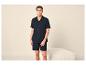 Mann in marineblauem Hemd und Shorts, stehend vor einem weißen Pouf.