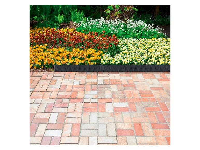 Eine Terrasse mit Fliesen und ein Blumenbeet mit gelben, roten und weißen Blüten.