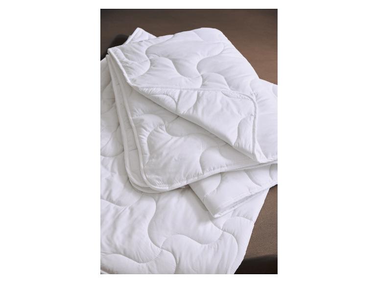 Weiße, gesteppte Decke oder Bettdecke gefaltet auf einer dunkelbraunen Oberfläche.