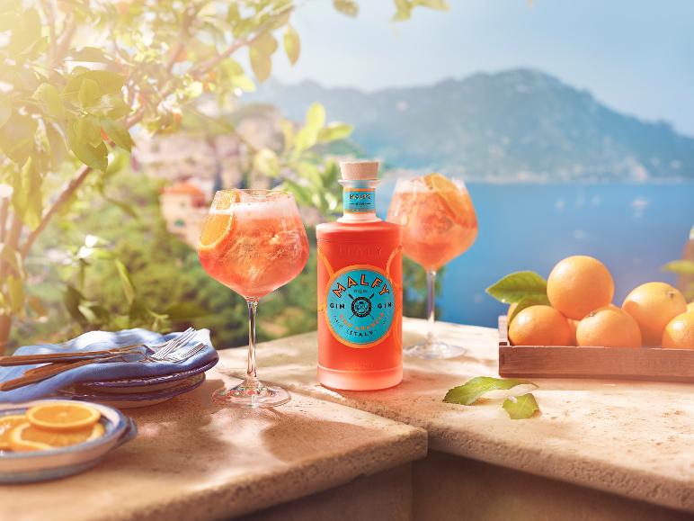 Orangengin-Flasche und Cocktails auf einer sonnigen Terrasse mit Meerblick.