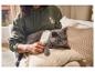 Frau bürstet Katze mit weißer Bürste, Katze ist grau, Frau trägt grünen Hoodie.