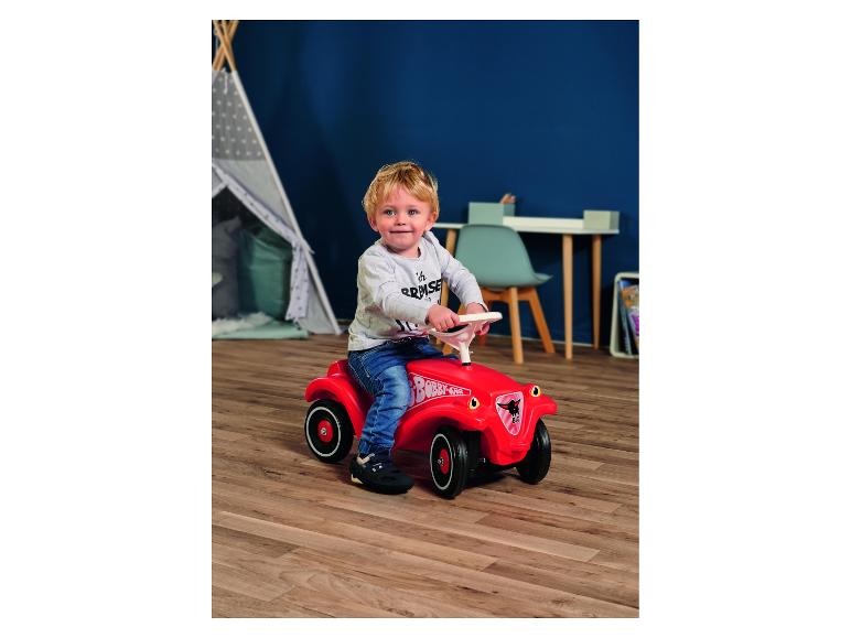 Kleinkind auf einem roten Rutschauto im Kinderzimmer.