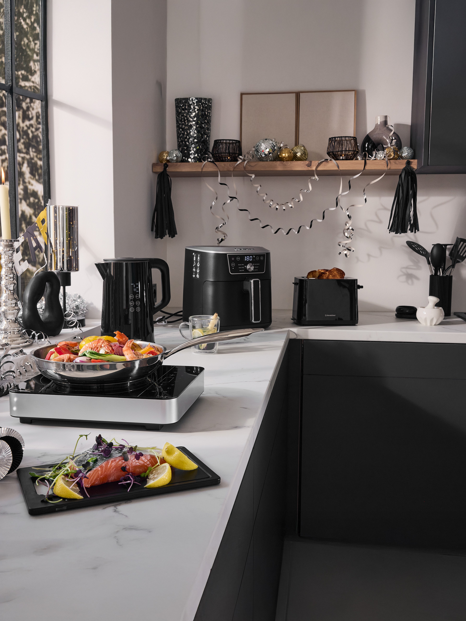 Küchenarbeitsplatte mit SilverCrest Heißluftfritteuse, Wasserkocher, Toaster und Küchenutensilien, festlich dekoriert.