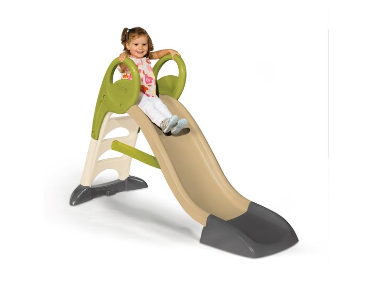 Lächelndes Mädchen rutscht eine beige-grüne Rutsche hinunter.