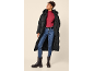 Frau in langem schwarzem Steppmantel, rotem Rollkragenpullover, blauen Jeans und schwarzen Stiefeln.