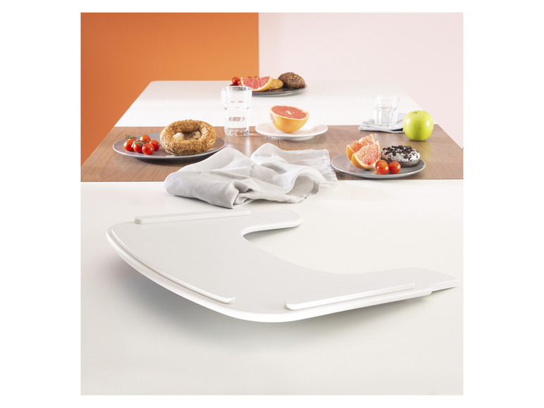 Ein weißes Tablett mit einem Donut, Grapefruit und Tomaten auf einem Holztisch.