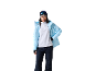 Frau in hellblauer Skijacke, weißem Fleece, dunkelblauer Skihose, grauer Mütze und Skibrille.