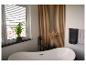 Modernes Badezimmer mit freistehender Badewanne, Holzlamellenwand und Grünpflanze.