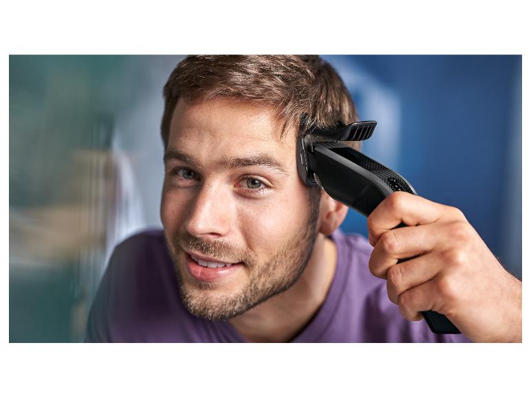 Junger Mann benutzt einen elektrischen Haarschneider, um sich die Haare zu schneiden.