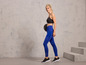 Frau in blauen Sportleggings und schwarzen Sportschuhen mit einem Gewicht in der Hand.