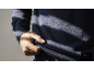 Nahaufnahme eines Mannes in einem dunkelblauen Strickpullover, der den gerippten Saum hält.