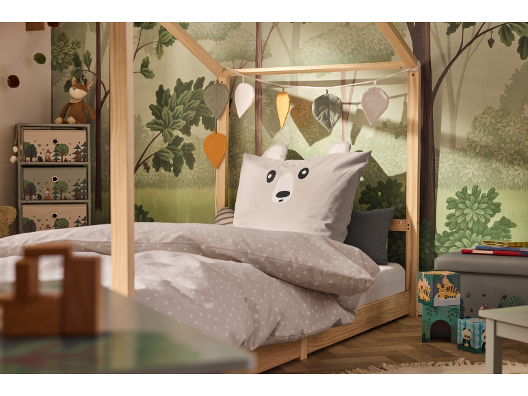 Kinderbett mit Waldtapete und Tierbettwäsche.