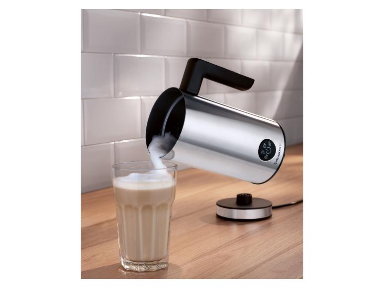 Silberner Silvercrest Milchaufschäumer auf einer Holztheke, der Schaum in ein Glas gießt.