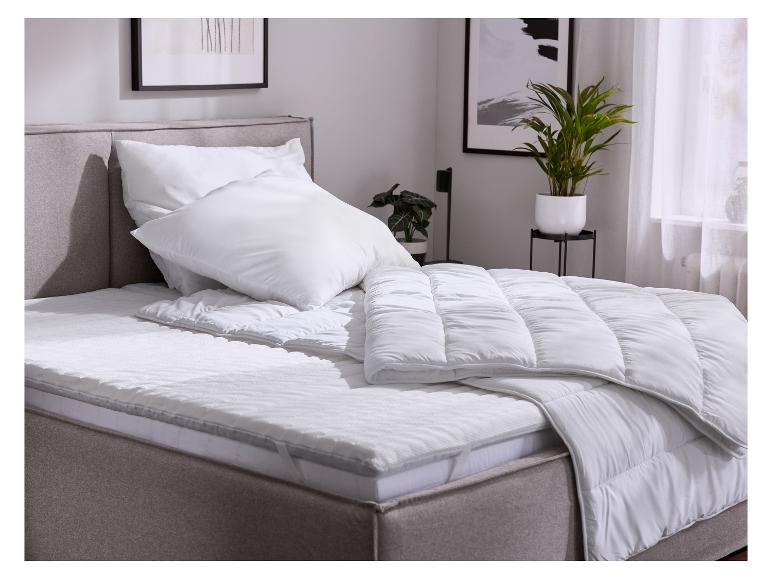 Bett mit weißer Bettwäsche, Kissen und Decke in einem Schlafzimmer mit Pflanzen.