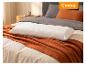 Weißes strukturiertes Kissen auf einer orangefarbenen Decke und grauer Bettwäsche in einem Schlafzimmer