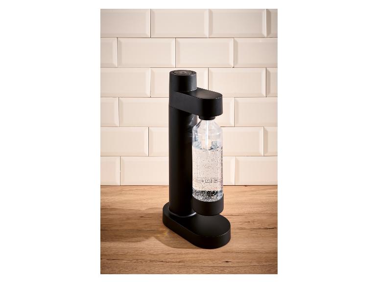Schwarzer Sprudelwasserbereiter mit einer Flasche kohlensäurehaltigem Wasser auf einer Holztheke.