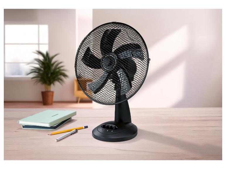 Schwarzer Tischventilator auf einem Holzschreibtisch mit Notizbüchern und Stiften, in einem hellen Raum.
