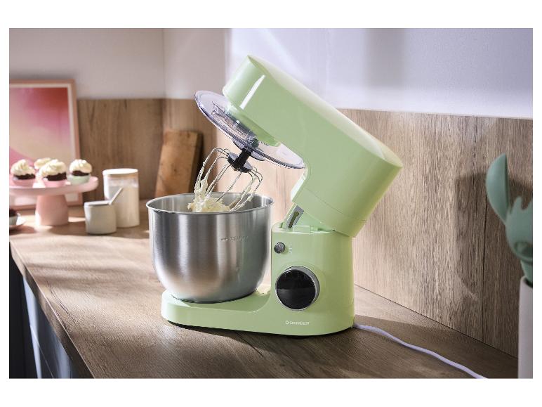 Hellgrüne Küchenmaschine mit Metallschüssel und Schneebesen auf einer Holzarbeitsplatte.