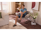 Mann in Shorts und Sandalen, sitzt in einem Sessel in einem modernen Wohnzimmer.