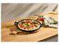 Gemüse-Pizza in einer schwarzen Gusseisenpfanne auf einem Holztisch mit Leinentuch.