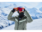 Skifahrer mit Helm, Skibrille und Sturmhaube, in grüner Jacke, in den Bergen.