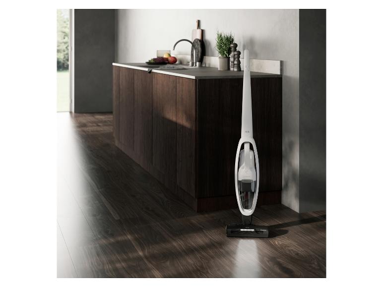 Weißer Akku-Staubsauger in einer modernen Küche mit dunklem Holzboden und Schränken.