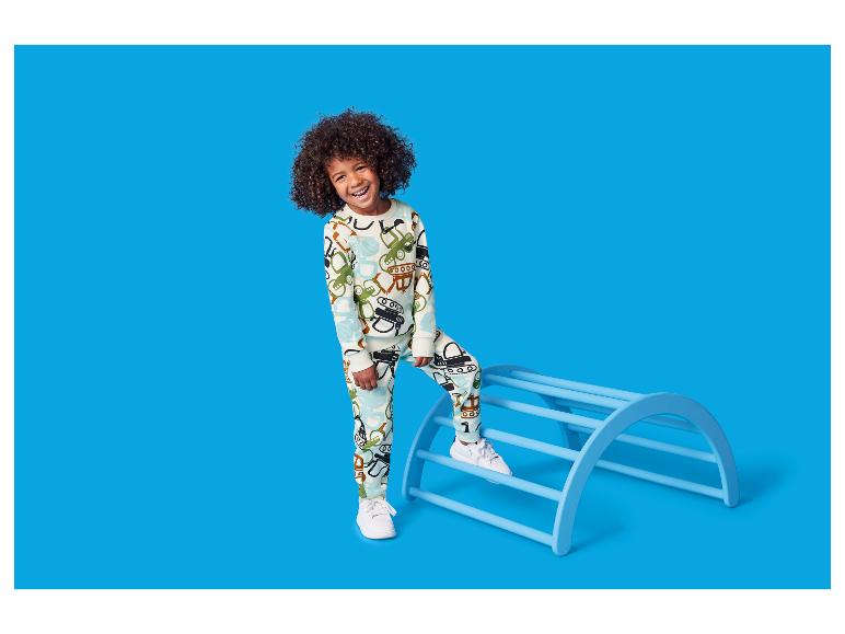 Glückliches Kind in Schlafanzug mit Fahrzeugaufdruck, das auf einem blauen Klettergerüst steht.