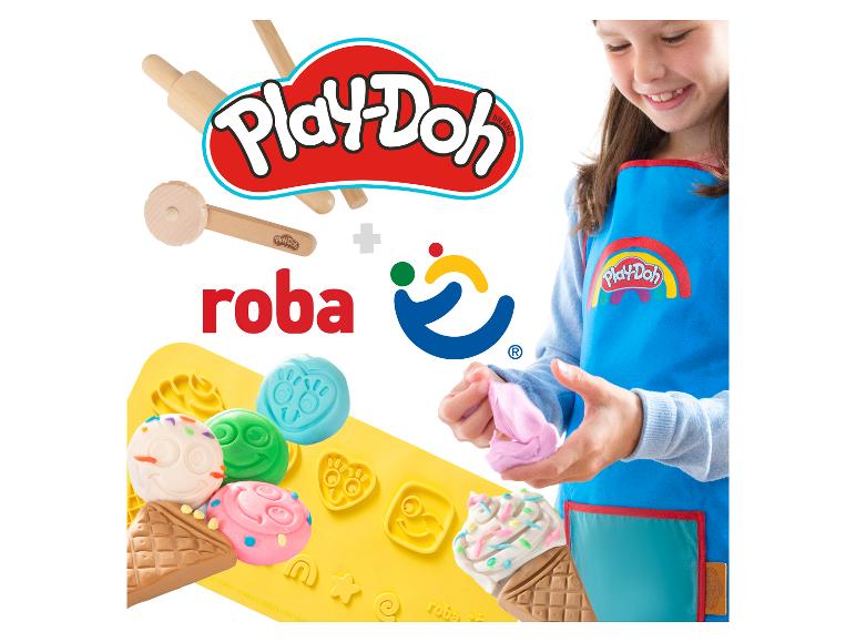 Lächelndes Mädchen in blauer Schürze knetet rosa Spielmasse, mit Holzwerkzeugen und Silikonformen.